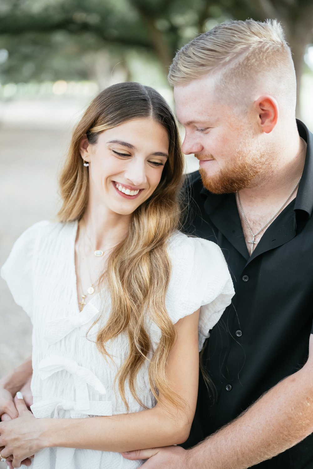 Close-up engagement portrait of a smiling couple embracing under Houston oak trees