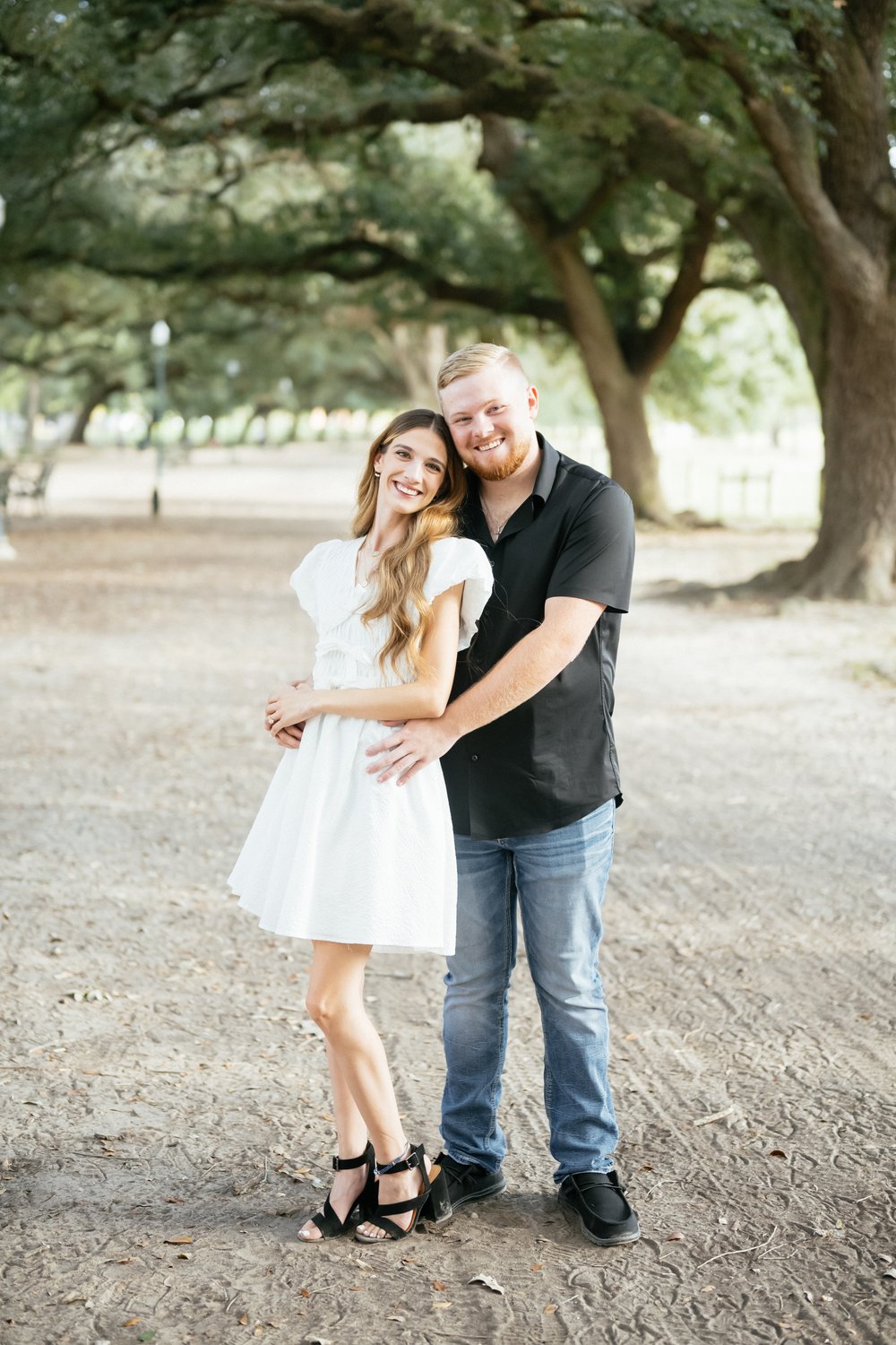 Engaged couple embracing beneath sprawling live oaks in a Houston park